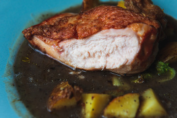 Cooked chicken fillet with crispy bronze skin in a soup with potato. Homemade dinner in a turquoise plate. Closeup.