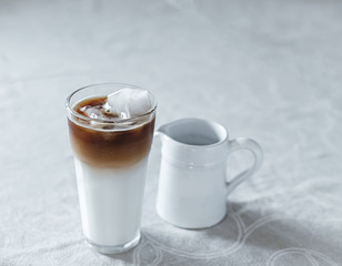 Iced coffee latte in a tall glass of milk with ice cubes on a clean and nice table, vintage, rustic, minimalistic look, no pouring, morning