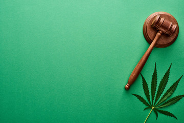 top view of green cannabis leaf near wooden gavel on green background with copy space