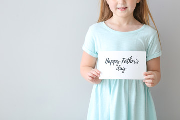 Cute little girl with greeting card for Father's Day on light background