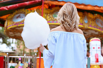 Woman with sweet cotton candy in amusement park, back view