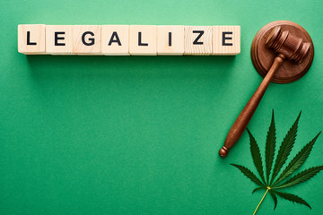 top view of green cannabis leaves and legalize lettering on wooden blocks near gavel on green...