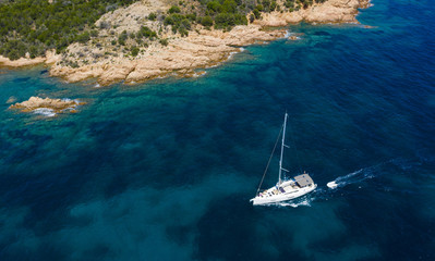 View from above, stunning aerial view of a sailboat sailing on a beautiful turquoise sea that bathes the green and rocky coasts of Sardinia. Emerald Coast Italy