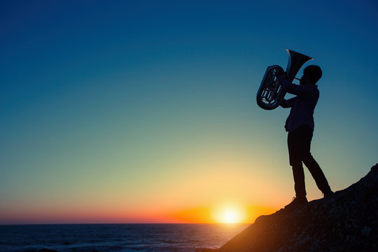 Silhouette of musician with tuba on the ocean beach during surreal sunset.