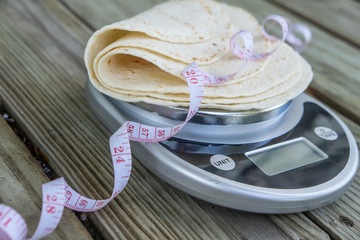 Low carb tortillas on a food scale with measuring tape on wooden background.