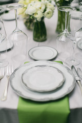 wedding reception table setting, fine china plates, green napkin hanging off table, silverware, wine glasses, and flower arrangments