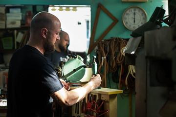 A male shoemaker riveting with an old rivet press machine at h.is workshop