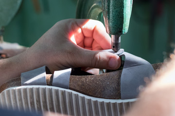 Close up of the hands of a male shoemaker riveting with an old rivet press machine.