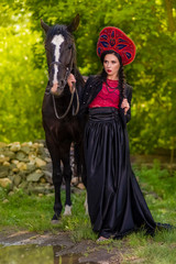 Model in Russian Kokoshnik Holding Thoroughbred Horse Against Nature Background.