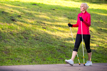 Portrait of Smiling Sportive Senior Woman Doing Nordic Walking in Park.