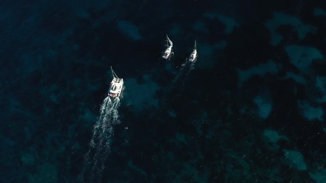 View from above, stunning aerial view of a catamaran and two sailboats sailing on a blue sea. Emerald Coast  Sardinia, Italy.