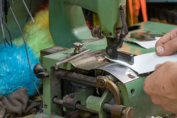 Close up of male shoemaker hands skiving leather with a vintage skiving machine.