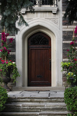 Fototapeta na wymiar front door of gothic style stone house with floral planters and flagstone steps