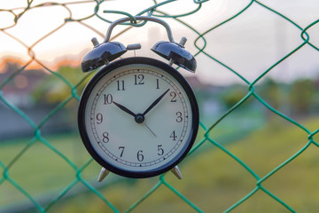 clack analog clock hanging on blurry green fence