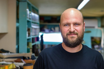 Portrait of a bald mand with beard, shoemaker looking camera at his workshop.