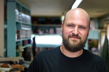 Portrait of a bald mand with beard, shoemaker looking camera at his workshop.