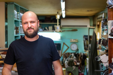 Fototapeta na wymiar Portrait of a bald mand with beard, shoemaker looking camera at his workshop.