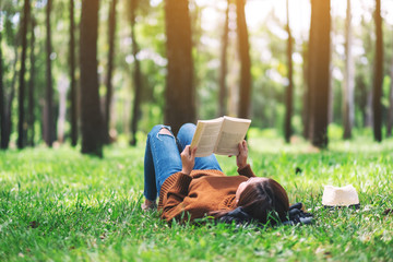 A beautiful Asian woman lying and reading a book in the park - obrazy, fototapety, plakaty