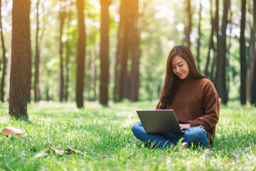 A beautiful asian woman working and typing on laptop keyboard while sitting in the park