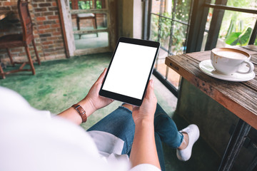 Mockup image of a woman holding black tablet pc with blank white desktop screen while sitting in cafe