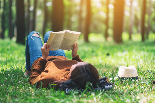 A beautiful Asian woman lying and reading a book in the park