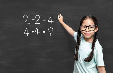 Little asian girl standing at blackboard with chalk in her hand near mathematics equation.