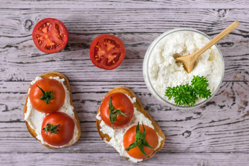 Toasted toast with fresh cottage cheese and tomatoes on a wooden table. Flat lay.