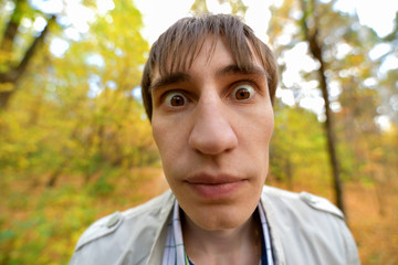 Portrait of a man with bulging eyes and a big nose in the autumn forest. The surprised expression of the dark-haired man. Horizontal photography