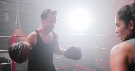 Female boxer with trainer using focus pads