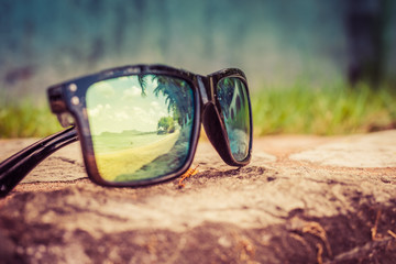 Fototapeta na wymiar Fashionable sunglasses. Sunglasses with mirrored lenses. Reflection of the beach and tropical palm trees in sunglasses