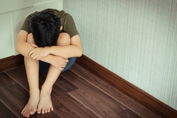 Young Asian preteen/teenage boy sitting at the corner of a room feeling lost. He has his face down and crying. Cyber Bullying, Teen problems, Loneliness, Traumatic, Stressed, frustrated and lost.