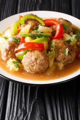 Tasty meatballs with pineapples and vegetables in sweet and sour sauce close-up on a plate. vertical