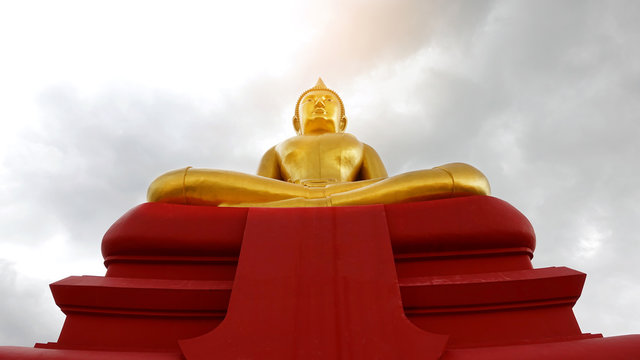 Statue of Luang Pho Sothon A large golden body on a red base on the sky background