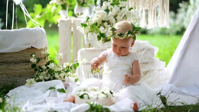 A little daughter in white dress puts the nameplate with the word one in the flowers. Holiday concept.