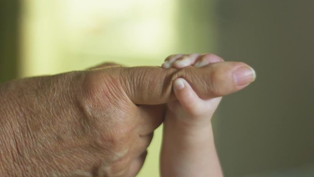 Slow motion of baby holding her grandfather's finger