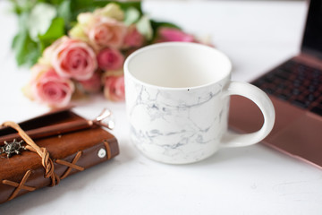 Womens workspace with laptop, bouquet of pink roses, a notebook, a pen and a cup of tea or coffee