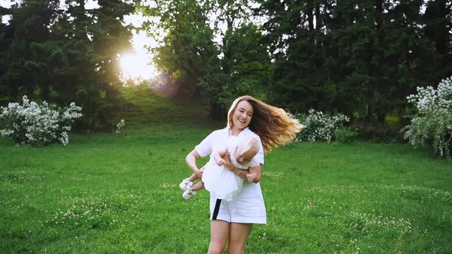 A young woman whirls with the baby in the park. The mother having fun whirls with the baby in outdoors in slowmo 120fps.