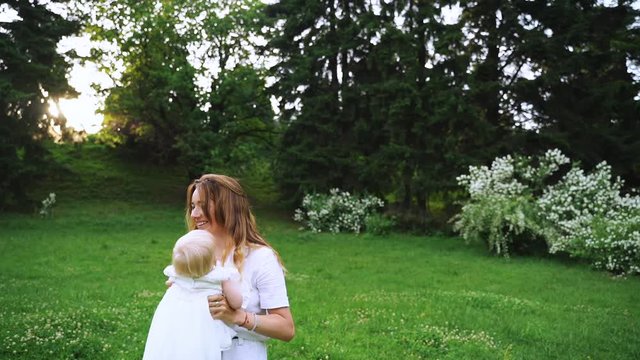 Young mother and her baby playing enjoying sunset in nature on summer day. happy family walking outdoors. The mother having fun tossing up the baby in the air. Slow Motion 120 fps,