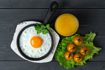 fried eggs in cast iron frying pan on white wooden stand with yellow cherry tomatoes and orange...