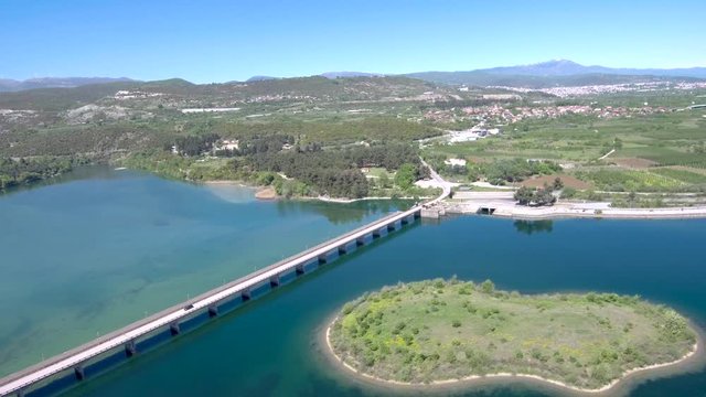 Aerial view of wide river with car bridge in a plain with crops, Aliakmonas river, Veria Greece, moving forward by drone