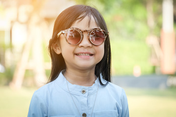 Asian child girl, smiling face, wearing a denim shirt and sunglasses, standing in an outdoor garden