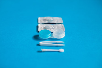 Blue color pair of contact lenses in blisters with blue contact lens case and tweezers on blue background