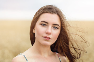 Fototapeta premium Portrait of the girl posing against the background of the wheat field in the warm summer evening