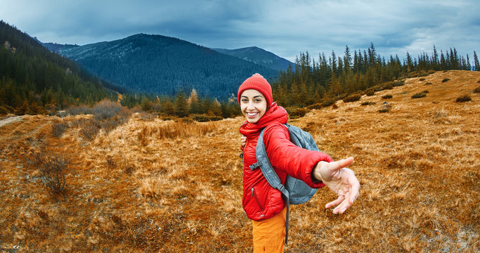 image of a young smiling woman hiker with small backpack standing on a mountain slope. Follow me, hiking, active and travel lifestyle concept.
