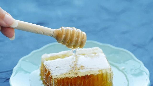 Natural Eco Food Concept. Hand holds spindle for honey. Sweet honeycombs in a plate