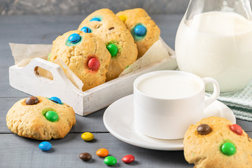 A cup of milk and cookies decorated with colorful jelly beans candies on a gray background. Children's breakfast snack.