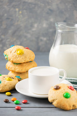 A cup of milk and homemade cookies decorated with colorful jelly beans candies on a gray table background. Copy space.