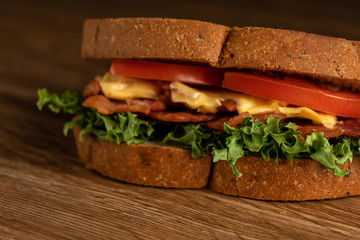 Sandwich with filling from lettuce, slices of fried bacon, tomato and cheese with whole wheat bread. wooden background. Macro photography.