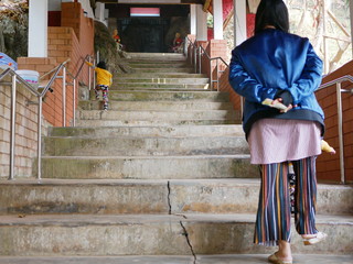 Little Asian baby girl, 2 years old, learning to climb up the stairs by herself, while having her mother watching from a far distance