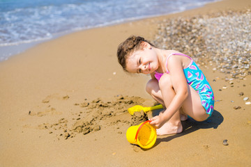 cute little girl playing with sand and toys on tropical beach on the background of the sea. Family vacation concept